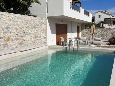 Bungaló blanco moderno con piscina y zona de estar bajo cielo azul.