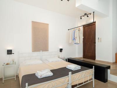 Dormitorio moderno con cama blanca, puerta de madera y banco oscuro.