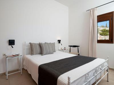 Dormitorio luminoso con cama doble, cojines a rayas, manta negra y ventana con vista al exterior.