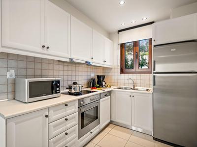 Cocina pequeña y moderna con gabinetes blancos, salpicadero de azulejos grises y electrodomésticos de acero inoxidable.