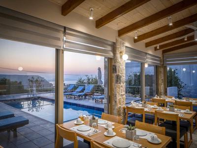 Zona pranzo con tavoli in legno con vista su piscina e tramonto sul mare.