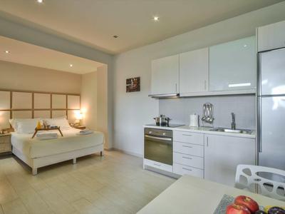 Chambre d'hôtel moderne avec kitchenette et lit double dans des couleurs claires.