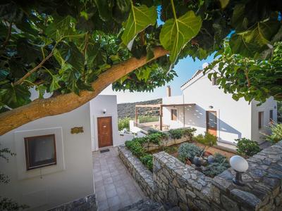 Cortile con edifici bianchi, sentieri in pietra e vegetazione rigogliosa sotto un cielo soleggiato