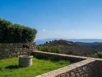 Un puits en pierre dans une cour herbeuse avec vue sur les collines sous un ciel bleu clair.