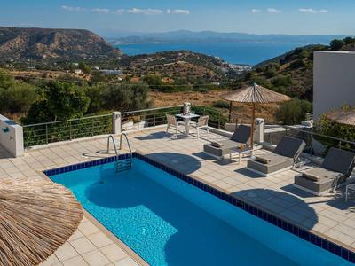 Piscine avec chaises longues et parasols offrant une vue sur les collines et la mer en arrière-plan.