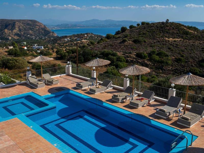 Piscine avec chaises longues et parasols donnant sur un paysage vallonné et la mer.