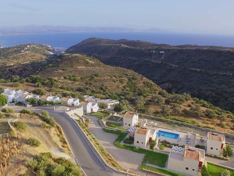 Paysage avec collines, routes et bâtiments près d'une zone côtière avec la mer en arrière-plan.