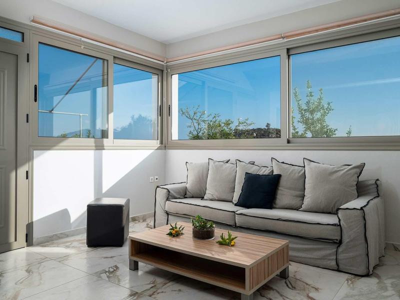 Coin lumineux avec canapé, table basse et grandes fenêtres donnant sur le ciel.