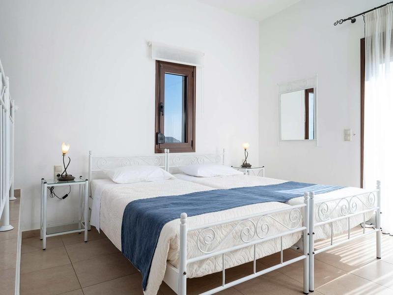 Chambre lumineuse avec lit en métal blanc, couverture bleue et petites tables de chevet.