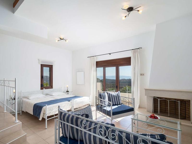 Chambre d'hôtel lumineuse avec lit double, canapé, cheminée et vue sur la mer.