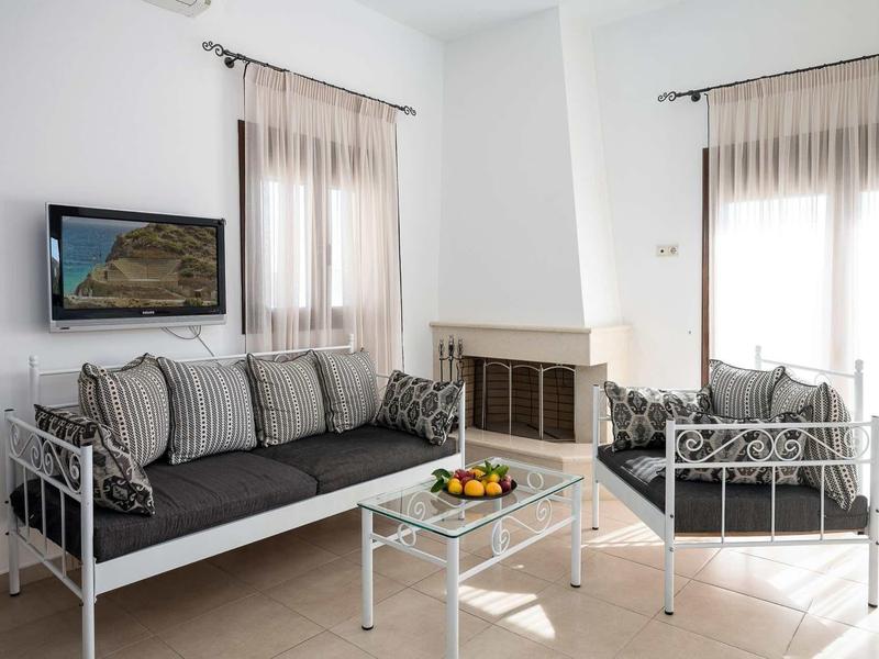 Salon avec deux canapés gris, table en verre, cheminée et télévision sur murs blancs.