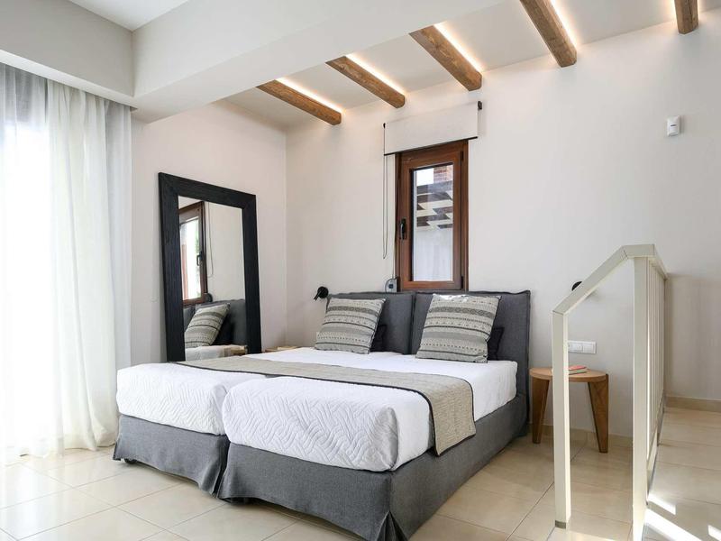 Chambre moderne et lumineuse avec lit double, grand miroir et plafond à poutres en bois.