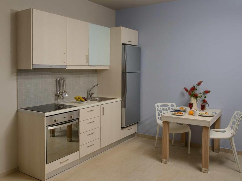 Cuisine compacte avec armoires en bois, four, cuisinière, réfrigérateur à côté d'une table à manger avec deux chaises.