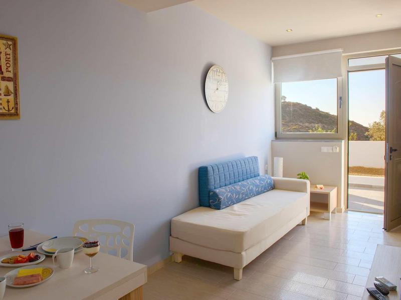 Chambre lumineuse avec canapé, table avec boissons et porte ouverte vers balcon avec vue sur la montagne.