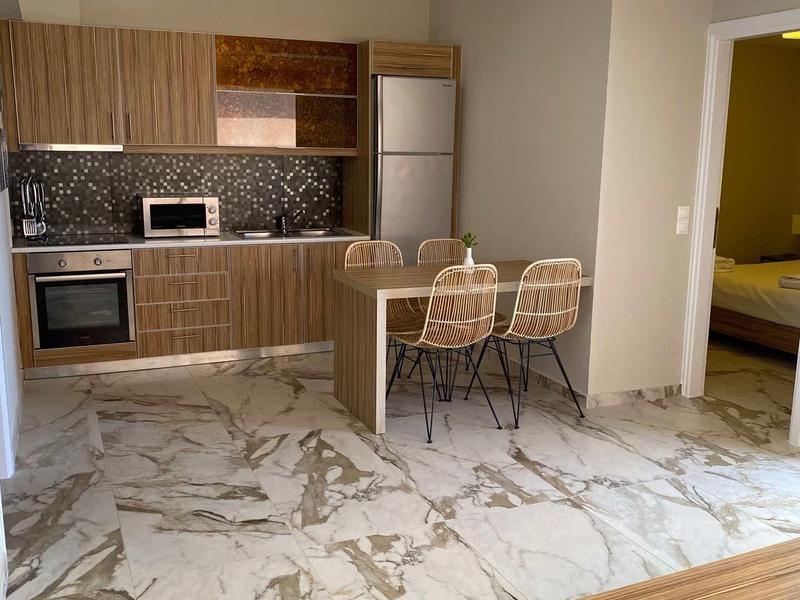 Cuisine moderne avec placards en bois, sol en marbre et petit coin repas avec deux chaises.