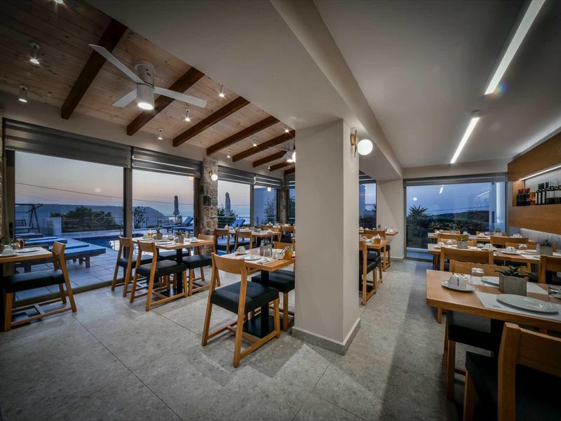 Restaurant chaleureux avec plafond à poutres en bois et grandes fenêtres offrant une vue nocturne.