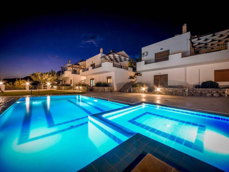 Piscine extérieure éclairée la nuit à côté de maisons de vacances blanches modernes.