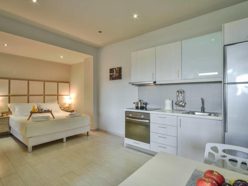 Chambre d'hôtel moderne avec kitchenette et lit double dans des couleurs claires.