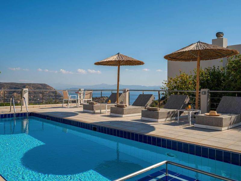 Piscine à débordement avec chaises longues et parasols face à la mer et aux montagnes.