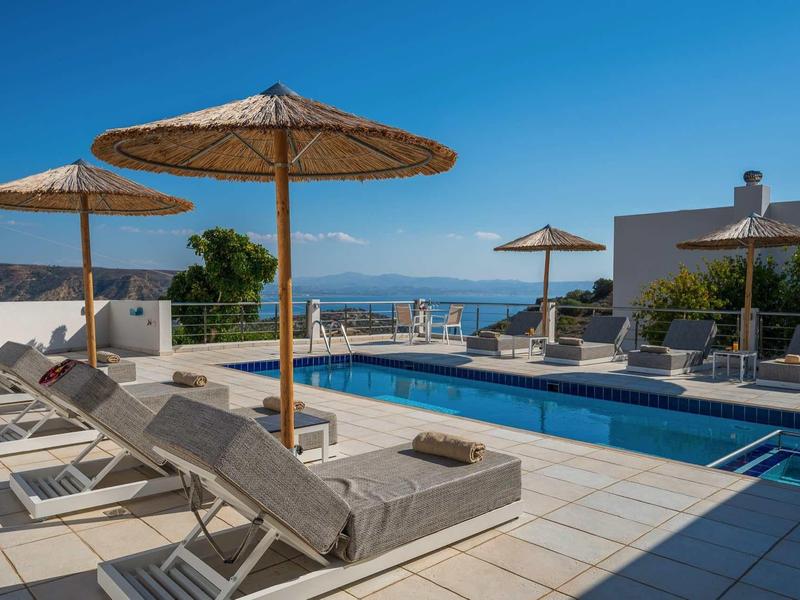Espace piscine avec chaises longues et parasols en paille sous un ciel bleu clair.