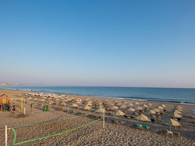 Spiaggia con numerosi ombrelloni e un'area giochi per bambini sul mare sotto un cielo sereno.