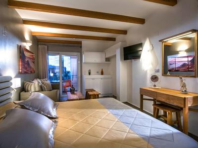 Cozy hotel room with a large bed, wooden beams, desk, and balcony with sea view.