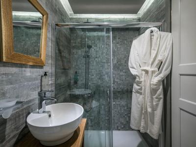 Modern bathroom with glass shower, white basin, wooden countertop, and bathrobe hanging on the wall.