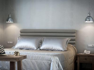 Modern bed with gray bedding, pillows, and wooden nightstands under wall lamps.