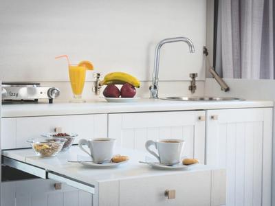 Compact kitchenette with white cabinets, coffee cups, juice, and fruit on the counter.
