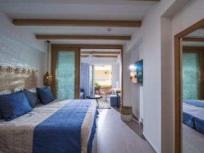 Comfortable hotel room with double bed, blue decor, and balcony opening to sea view.