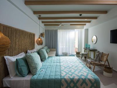 Hotel room with twin beds, turquoise bedding, wooden accents, and a balcony with curtains.
