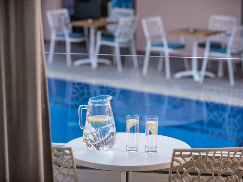 Glass pitcher and two glasses with water on a table overlooking a blue pool.