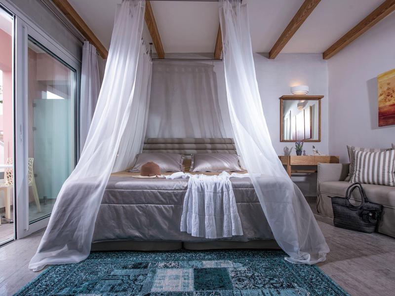 Cozy bedroom with canopy bed, sheer curtains, blue rug, and balcony with outdoor seating.