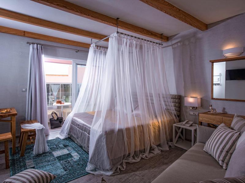 Cozy hotel room with a canopy bed, seating area, and balcony view under wooden beams.