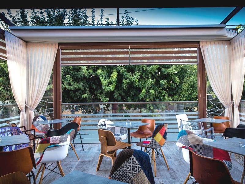 Outdoor hotel terrace with modern chairs, tables, and curtains overlooking greenery.