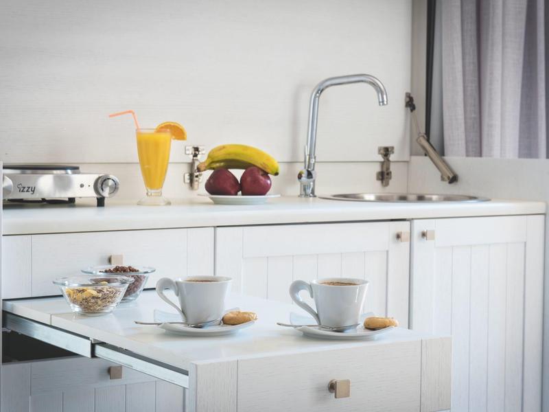 Compact kitchenette with white cabinets, coffee cups, juice, and fruit on the counter.