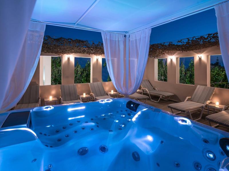 Luxury outdoor jacuzzi area at night with soft blue lighting and lounge chairs under white canopy.