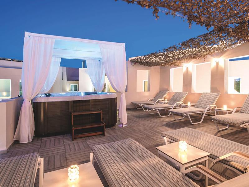 Outdoor lounge with jacuzzi and white sunbeds under a dusk sky at a hotel.