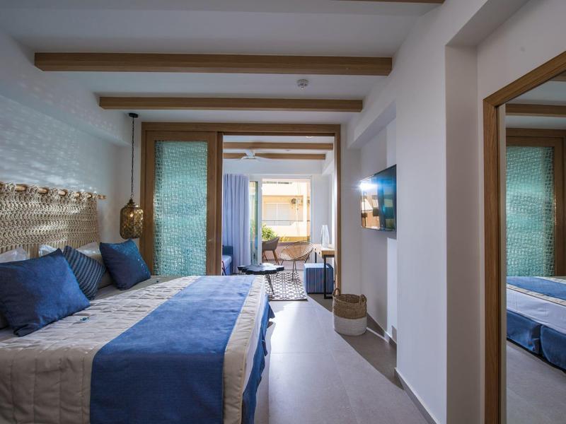 Comfortable hotel room with double bed, blue decor, and balcony opening to sea view.