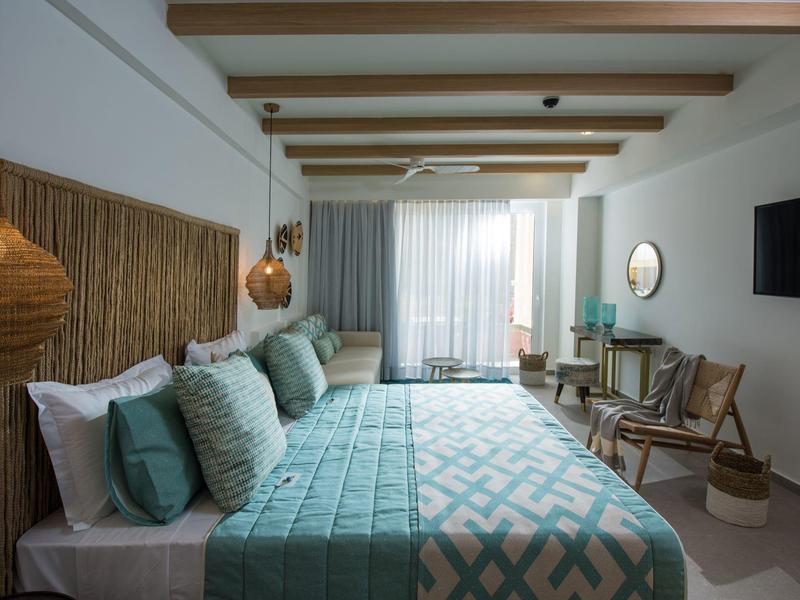 Hotel room with twin beds, turquoise bedding, wooden accents, and a balcony with curtains.