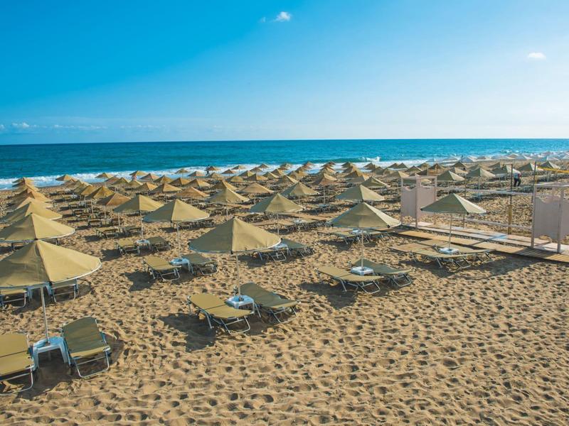 Sandy beach with rows of closed straw umbrellas and empty lounge chairs by the sea.