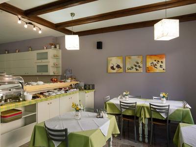 Jadalnia hotelowa z nakrytymi stołami i bufetem przy fioletowej ścianie.