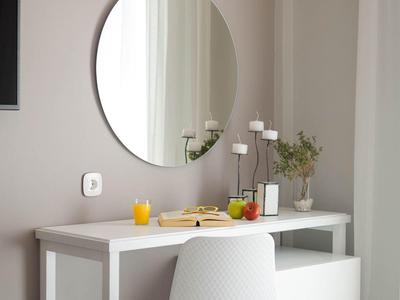 Okrągłe lustro zawieszone nad białym biurkiem z krzesłem i kapeluszem na łóżku.