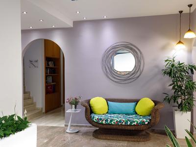 Przytulny salon hotelowy z kolorową ławką, roślinami i okrągłym lustrem na fioletowej ścianie.