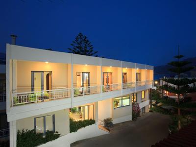 Hotel oświetlony nocą z balkonami, otoczony drzewami pod ciemnym niebem.