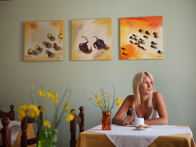 Kobieta siedzi przy nakrytym stole w pokoju z obrazami na ścianie.