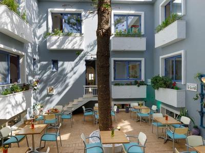 Dziedziniec z niebieskimi poduszkami na krzesłach, stołami i drzewem pośrodku nowoczesnego hotelu.