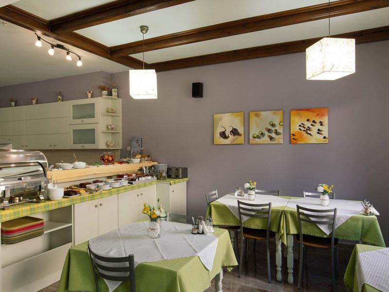 Jadalnia hotelowa z nakrytymi stołami i bufetem przy fioletowej ścianie.