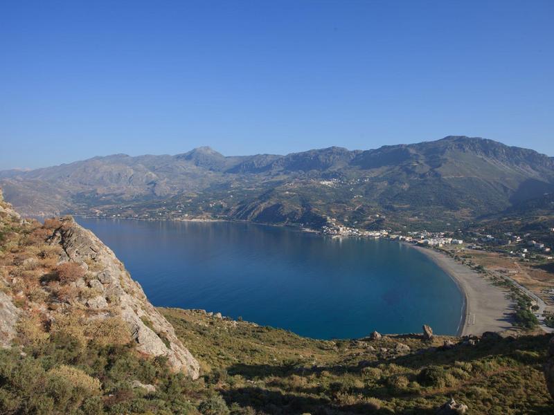 Zatoka w kształcie półksiężyca z plażą i wzgórzami pod jasnoniebieskim niebem.