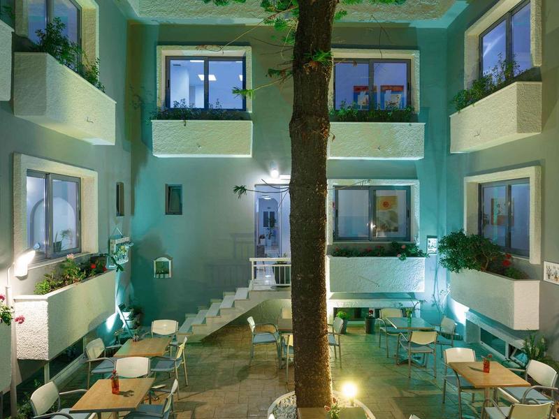 Dziedziniec hotelowy z stolikami, krzesłami i dużym drzewem w centrum nocą.